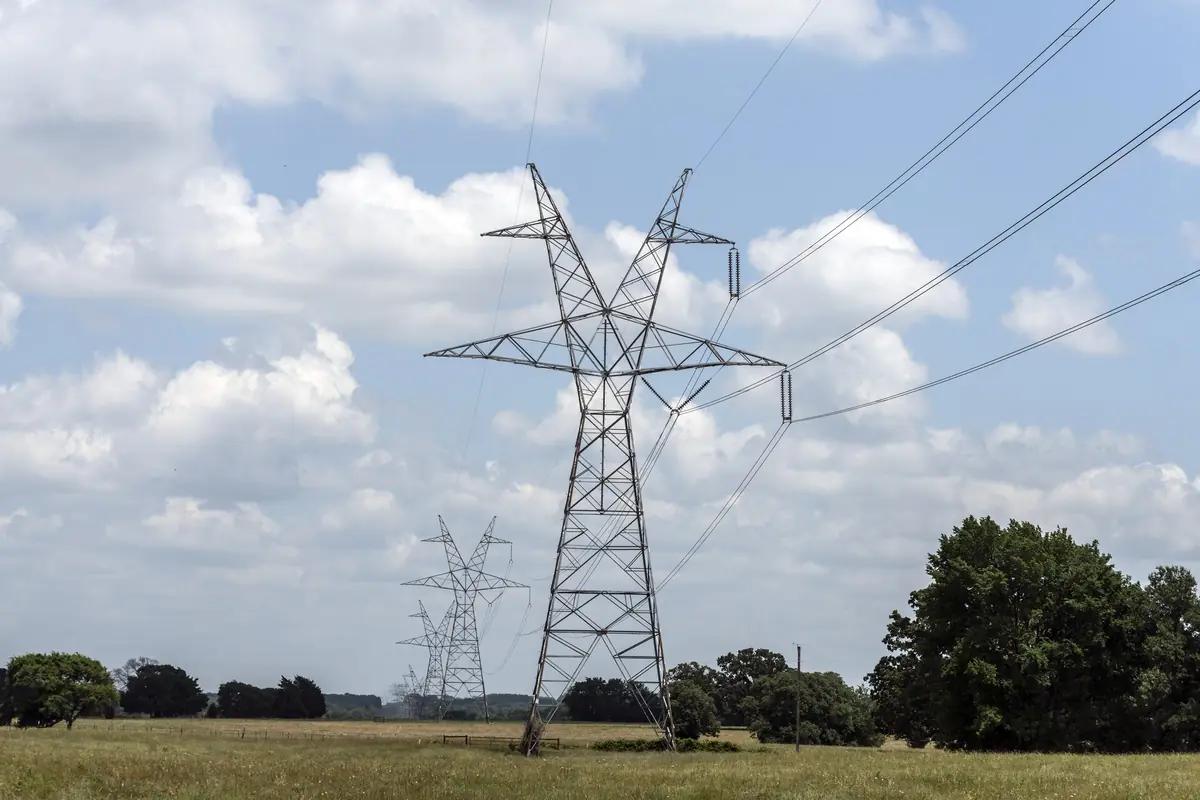High-voltage transmission towers crossing a green pasture under a cloudy blue sky