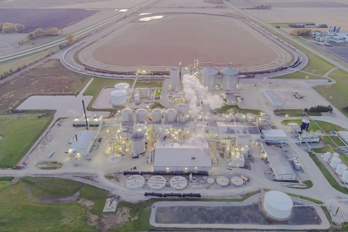 Aerial view of an ethanol plant with storage tanks, grain bins and a rail loop at dusk